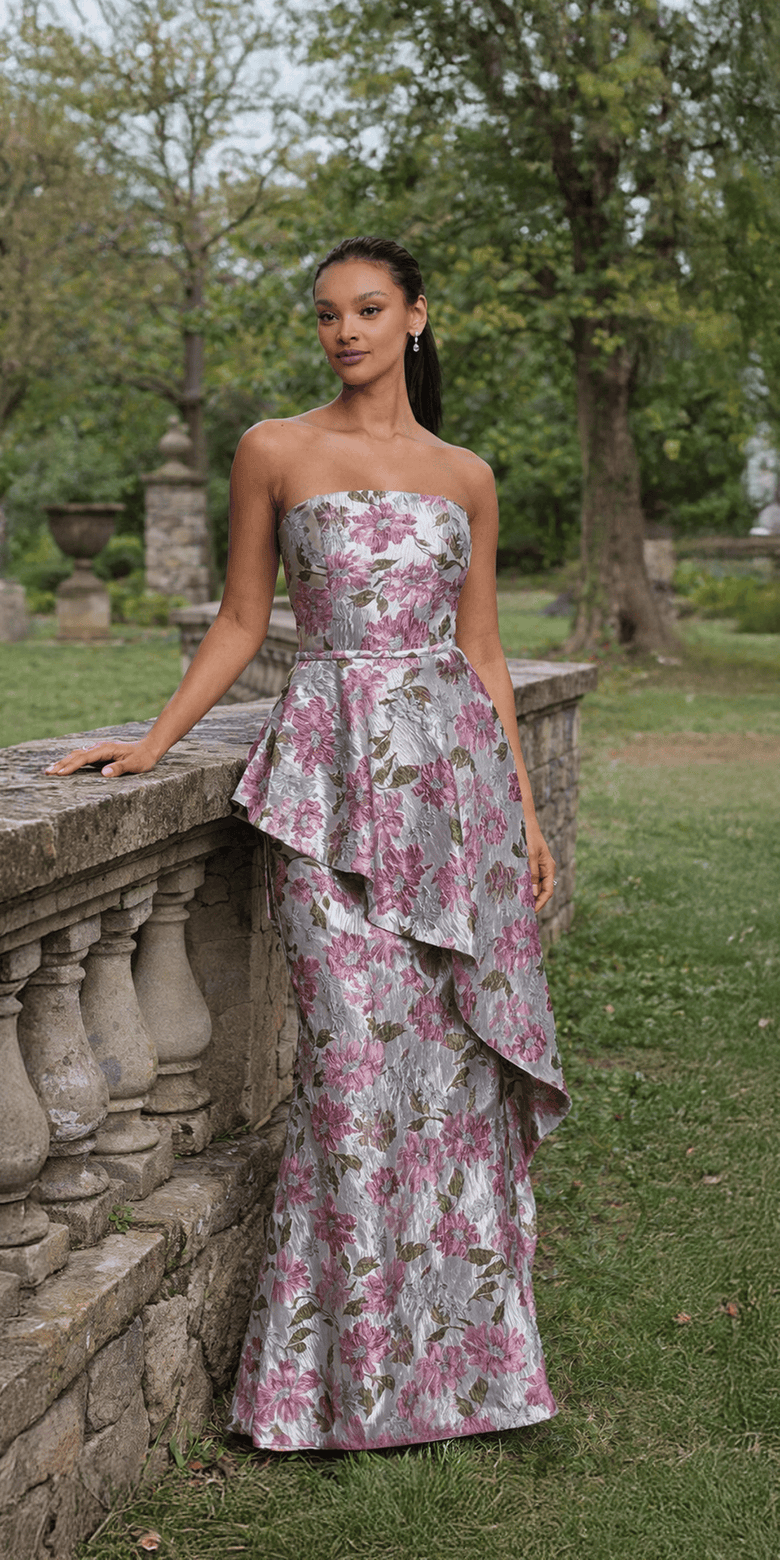 Woman in a floral strapless gown standing outdoors in a garden setting.